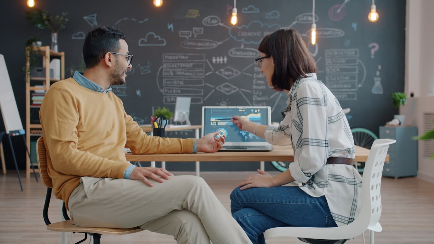 Two colleagues in a friendly discussion, pointing at a laptop screen together